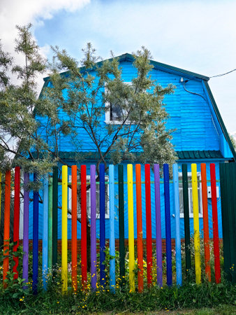 A bright blue house stands behind a colorful wooden fence in a sunny, lively neighborhood, with trees adding greenery to the scene.の写真素材
