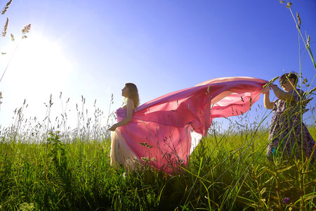 Wind plays with colorful fabric as two women enjoy a sunny day in a grassy field during the golden hourの写真素材