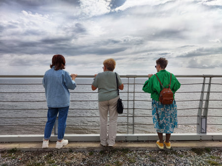 Three friends enjoying a peaceful moment by the waterfront under a cloudy skyの写真素材