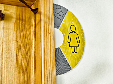 A bright yellow restroom sign featuring a woman symbol hangs on a wooden wall in a contemporary space.の写真素材