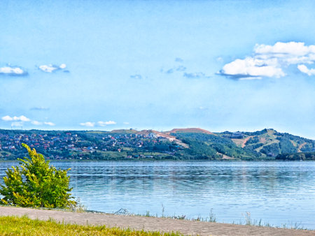 Calm waters reflect the blue sky as hills with greenery rise in the background, creating a peaceful...