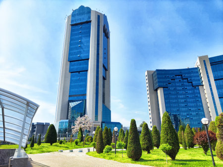 Tall buildings rise against a clear blue sky, surrounded by neatly trimmed trees and lush gardens in Tashkent, emphasizing urban development.の写真素材