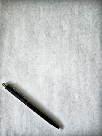 A blank sheet of parchment lies on a smooth surface with a pen placed beside it, inviting inspiration and creativity.の写真素材