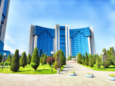Tall blue buildings rise amidst well-kept gardens and trimmed trees, showing the beauty of modern...
