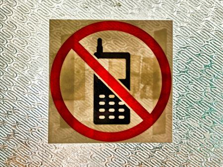 A clear warning sign shows a crossed-out cell phone symbolizing restriction on phone use in a specific location, emphasizing rules for safety.の写真素材
