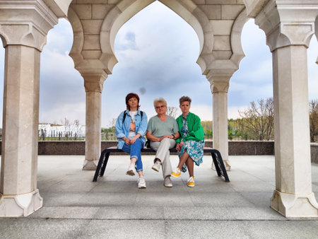 Three women sitting under an architectural archway in a scenic outdoor location during early afternoonの写真素材