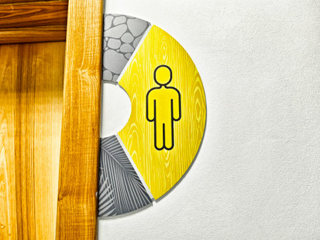 A distinctive restroom sign shows a yellow icon of a man, set against a stylish backdrop, placed near a wooden frame.の写真素材