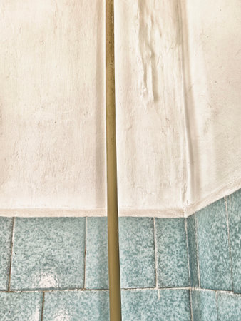 A tall, slim pole stands against a light textured wall. The background features pale tiles that add...