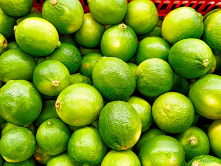 Bright green limes fill a red basket at an outdoor market on a sunny afternoon, ready for customers to buy.の写真素材