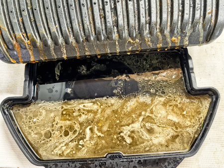 A grill tray shows significant oil and grease accumulation after cooking, with residue visible in the bottom compartment.の写真素材
