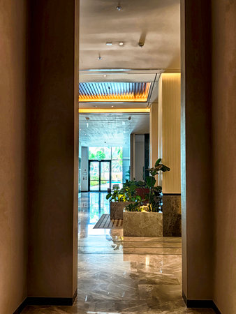 A spacious hotel lobby features elegant marble flooring, vibrant green plants, and large glass doors inviting natural light.の写真素材