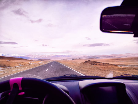 Vehicle view shows an open highway stretching through a rugged mountainous region under a clear sky,...
