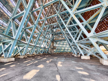 An abandoned building features complex blue beams and shadows on the ground, with sunlight streaming through at midday, creating a striking scene.の写真素材
