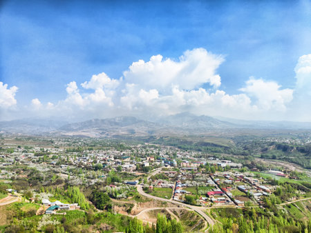 A scenic landscape shows a lush valley dotted with houses and roads beneath a clear blue sky with fluffy clouds.の写真素材