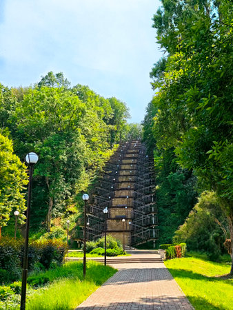 Visitors stroll along a path lined with lamps, surrounded by lush greenery and a striking incline on a sunny day.の写真素材