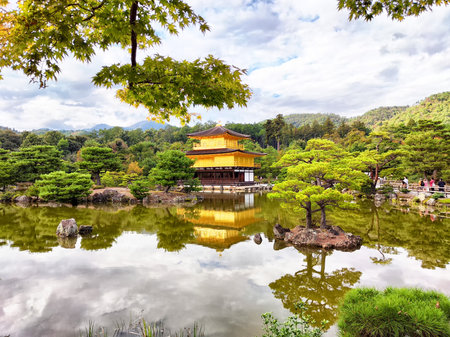 Golden Pavilion stands majestically on the water, embraced by vibrant trees and hills in Kyoto, Japan on a sunny afternoon.の写真素材