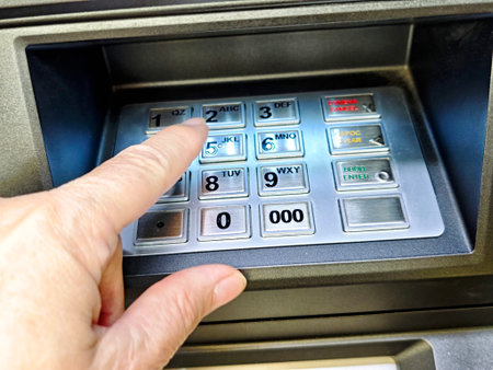 A hand is pressing a button on an ATM keypad, indicating a user performing a banking transaction for cash withdrawal or balance inquiry.の写真素材
