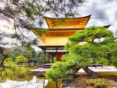 Golden Pavilion stands gracefully by the calm pond, surrounded by green trees and serene landscapes in Kyoto.の写真素材