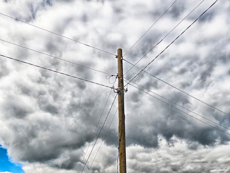 A wooden utility pole stands against a backdrop of dark, swirling clouds, indicating an approaching storm in a rural setting.の写真素材