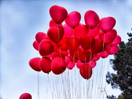 A vibrant display of heart-shaped balloons in red hues fills the sky, symbolizing joy and love during a festive gathering.の写真素材