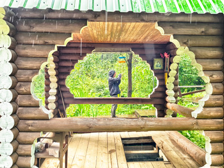 Slobodskoy, Russia - August 10, 2025: In Slobodskoy, Kirov region, two people are capturing moments in a wooden gazebo surrounded by lush greenery and light rain.のeditorial素材