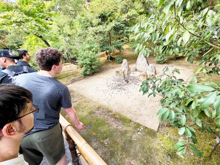 Kyoto, Japan - October 27, 2024: A group of tourists admires historic stone sculptures surrounded by lush greenery in a peaceful Kyoto garden setting.のeditorial素材