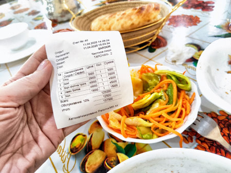 Tashkent, Uzbekistan - April 11, 2025: A person holds a receipt showing various traditional dishes served in Tashkent, highlighting local cuisine and prices.のeditorial素材