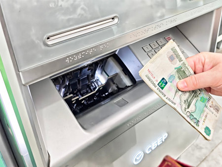 Maikop, Russia - June 04, 2025: A hand is shown reaching for cash from an automated machine in a banking area, highlighting the process of withdrawing funds.のeditorial素材
