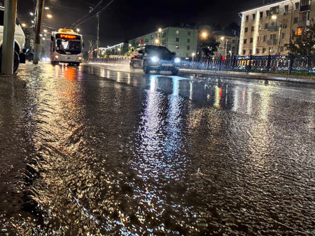 Kirov, Russia - August 30, 2025: Rainwater collects on the street, creating reflections of lights while cars and a bus drive through the wet pavement at night.のeditorial素材