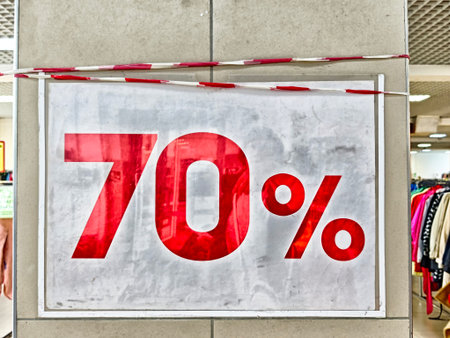 Kirov, Russia - September 10, 2025: A large red sign displays a 70 percent discount in a retail setting with colorful clothing racks nearby.のeditorial素材