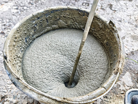Cement is being mixed in a bucket using a drill, preparing for construction tasks at a work site.の写真素材