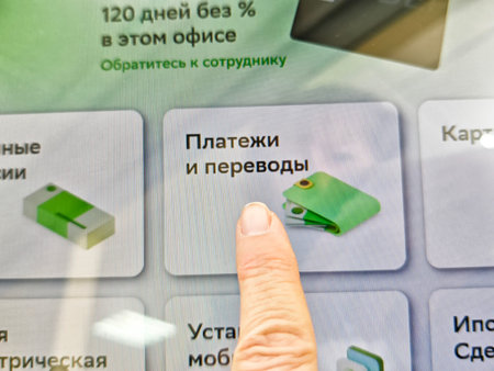 Kirov, Russia - August 26, 2025: A hand interacts with a payment and transfer option on a touch screen in a contemporary office environment.のeditorial素材