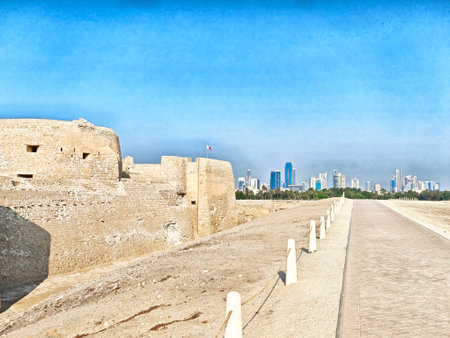 A historical fort stands alongside a modern skyline in Manama, Bahrain, under a clear blue sky, showing the contrast between past and present.の写真素材