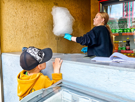 Kirov, Russia - September 10, 2025: A joyful child looks up eagerly while a vendor makes cotton candy at a fairground stand in bright sunlight.のeditorial素材