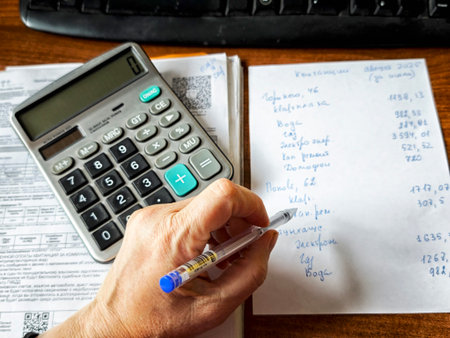 Kirov, Russia - August 15, 2025: A person is writing on a notepad while using a calculator to manage financial records in a well-lit workspace.のeditorial素材