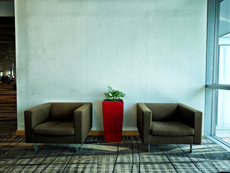 Two simple brown chairs are placed next to a red planter with a green plant inside.の写真素材