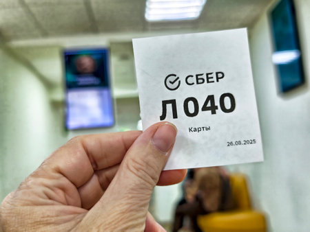 Kirov, Russia - August 26, 2025: A person holds a ticket showing their number while waiting for service at a bank on a busy day.のeditorial素材