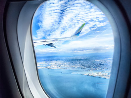 Bright clouds scatter across a clear blue sky while a city and coastline appear below from an...