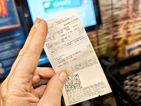 Kirov, Russia - August 06, 2025: A hand holds a grocery store receipt with detailed transaction information and a QR code in a busy shopping environment.のeditorial素材