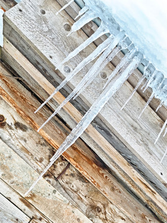 Icicles hang from the edge of a wooden roof, showing winter hazards and highlighting the dangers of...