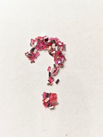 Minimal abstract composition with a question mark formed from pink decorative crystals on white...