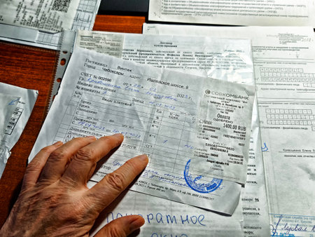 Kirov, Russia - November 12, 2025: Hand is seen holding several documents and receipts on a wooden...