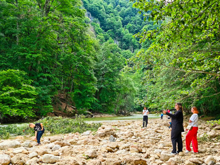 Maikop, Russia - June 05, 2025: Visitors explore the rocky riverbed of Guam Gorge in Adygea, surrounded by lush green trees and dramatic cliffs under clear skies.のeditorial素材