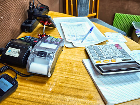 Kirov, Russia - November 10, 2025: A wooden desk in an office shows various calculators, phones, papers, and pens used during work tasks.のeditorial素材