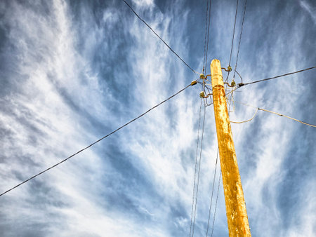 Wooden and concrete utility poles support power lines against a clear blue sky, showcasing critical infrastructure for energy distribution.の写真素材