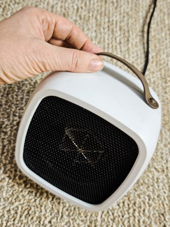 A person holds a small electric space heater designed for indoor use during cold months. This device provides warmth and comfort.の写真素材