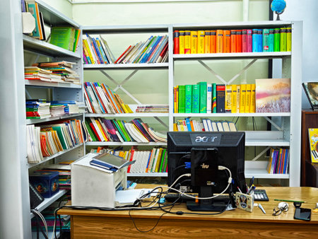 Kirov, Russia - November 05, 2025: A room has shelves with many books arranged by color and a desk with a computer and office supplies.のeditorial素材