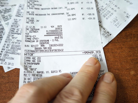 Kirov, Russia - January 05, 2025: Close up view of hands holding long grocery store receipt with food items and prices, expense tracking, budgeting, inflation and household finance conceptのeditorial素材