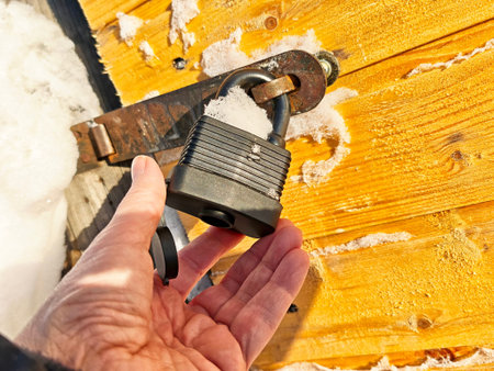 A hand is about to touch a black padlock on a wooden door. Snow covers part of the lock and...