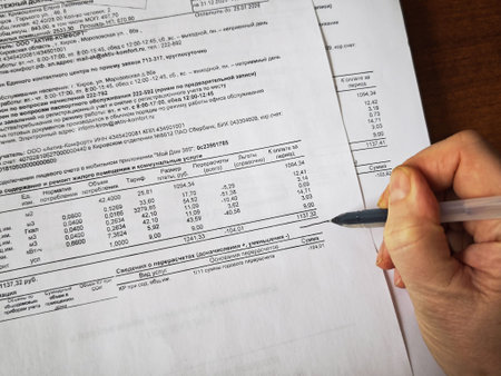 Kirov, Russia - January 16, 2026: A person is reviewing utility bills and payment documents while calculating household expenses at a desk.のeditorial素材